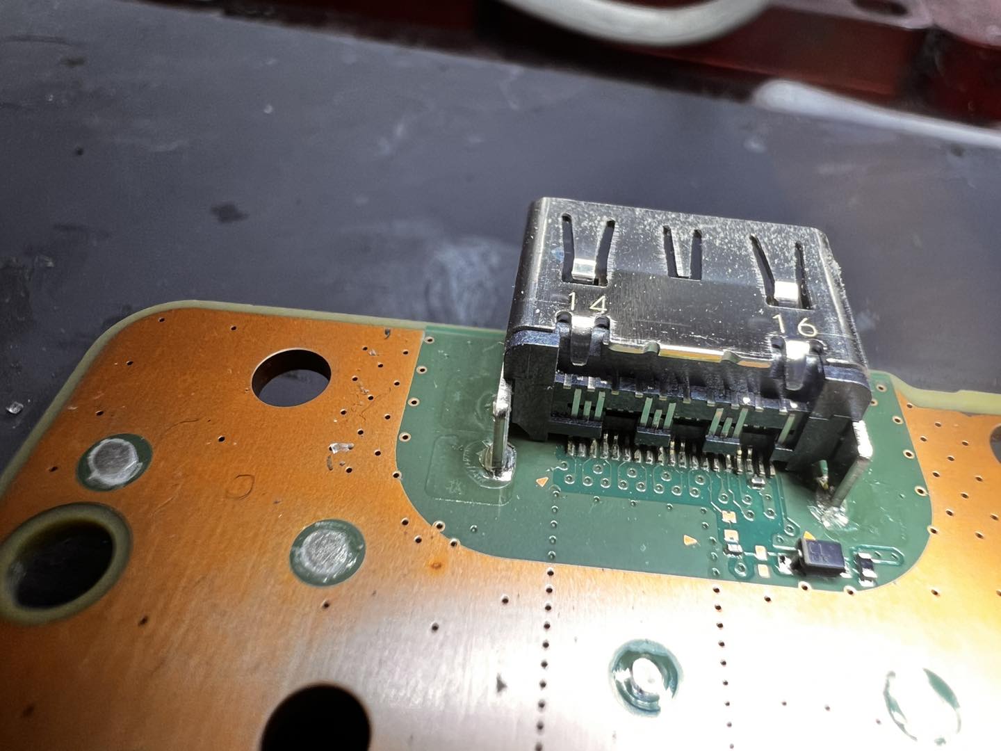 Microscope view of a damaged HDMI port still in place — cracked solder joints visible